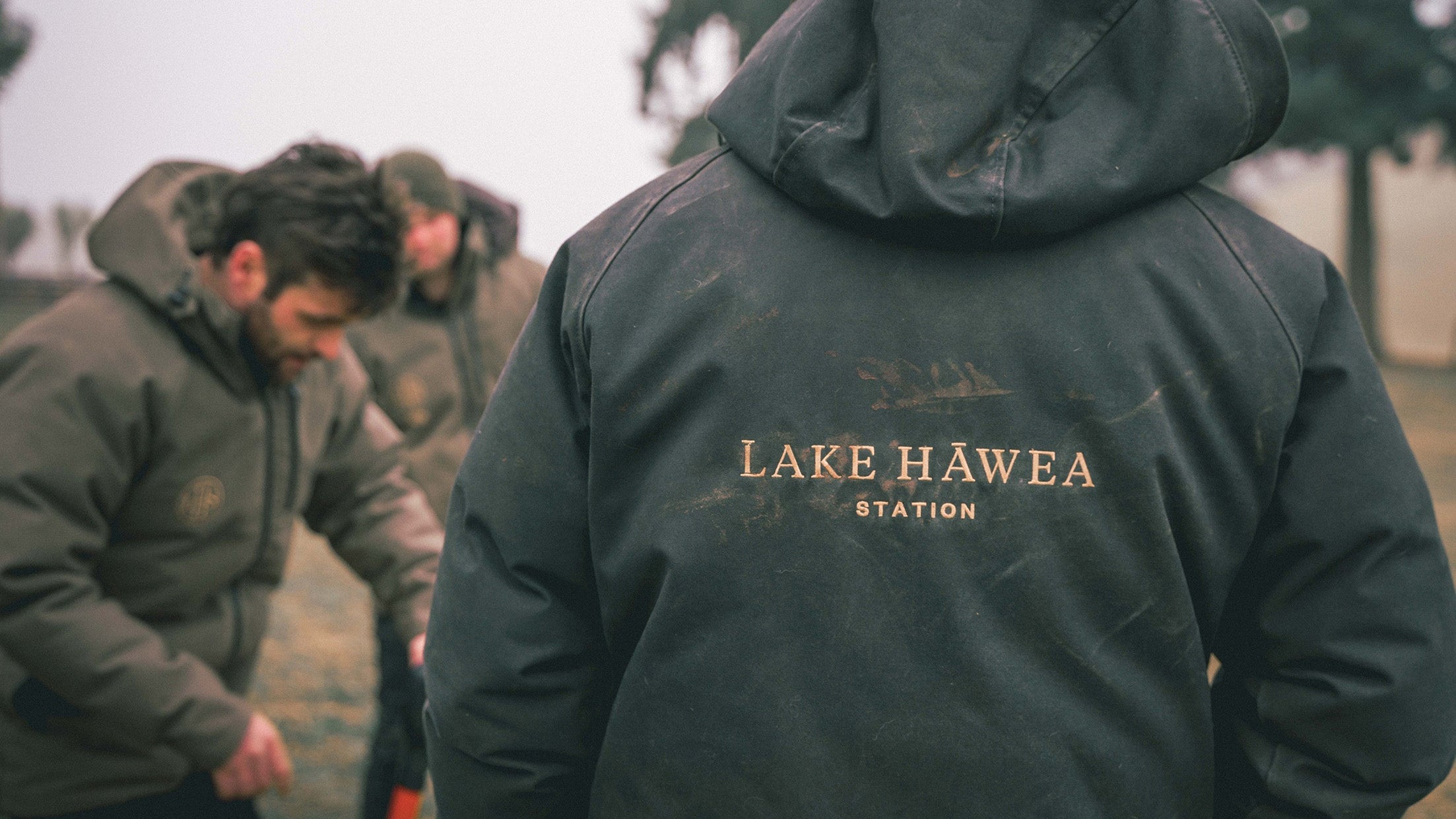 Person wearing a dark green jacket with 'Lake Hawea Station' branding, standing outdoors.